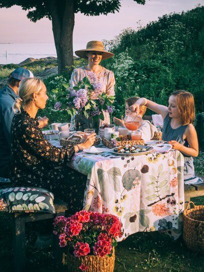 A group of people enjoying a scenic outdoor picnic with flowers and local food, embodying the "Finnish joy" (ilo) of summer activities in Helsinki.