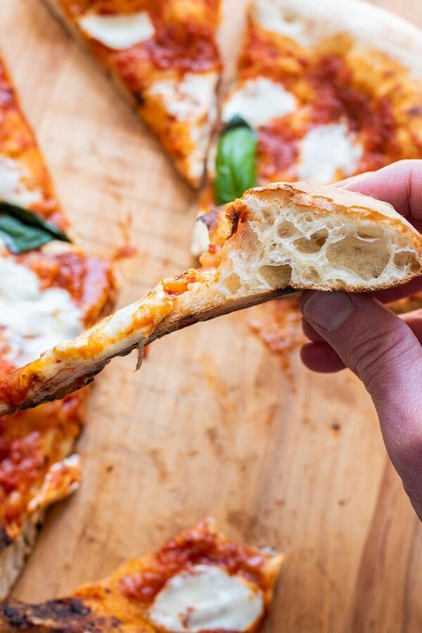 A hand holding a fresh slice of pizza, highlighting the diverse and budget-friendly street food options available for urban explorers in Finland