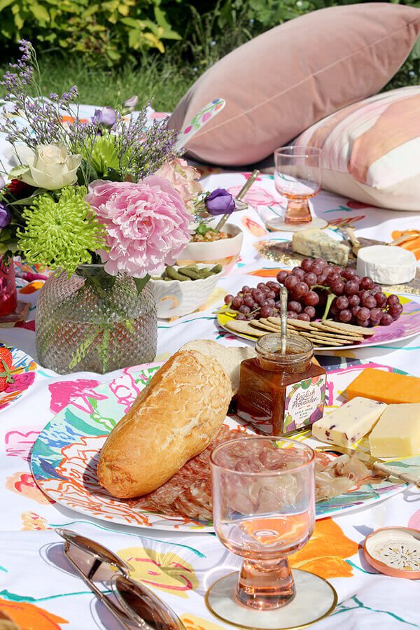 An aesthetic summer picnic spread on a floral blanket with fresh bread, cheese, grapes, and pink peonies, embodying the "Finnish joy" (ilo) of outdoor dining in Helsinki.