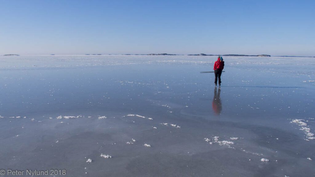 A person ice skating on the vast, mirror-like frozen Baltic Sea in the Helsinki archipelago, a breathtaking and unique winter activity in Finland.