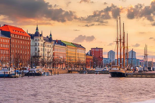 Historic sailing ships docked at North Harbor (Pohjoisranta) in Helsinki during a vibrant sunset, with colorful 19th-century architecture in the background.