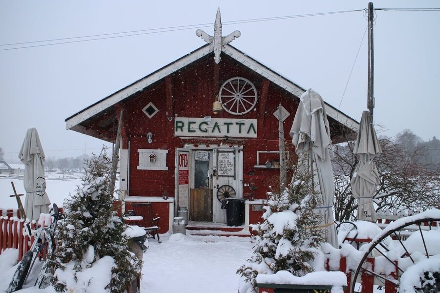 The iconic red wooden Cafe Regatta in Helsinki covered in snow, a cozy traditional spot for winter treats by the sea.