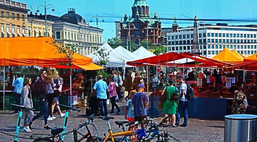 Vibrant Kauppatori Market Square in Helsinki during summer with orange stalls, tourists, and the Uspenski Cathedral in the background.