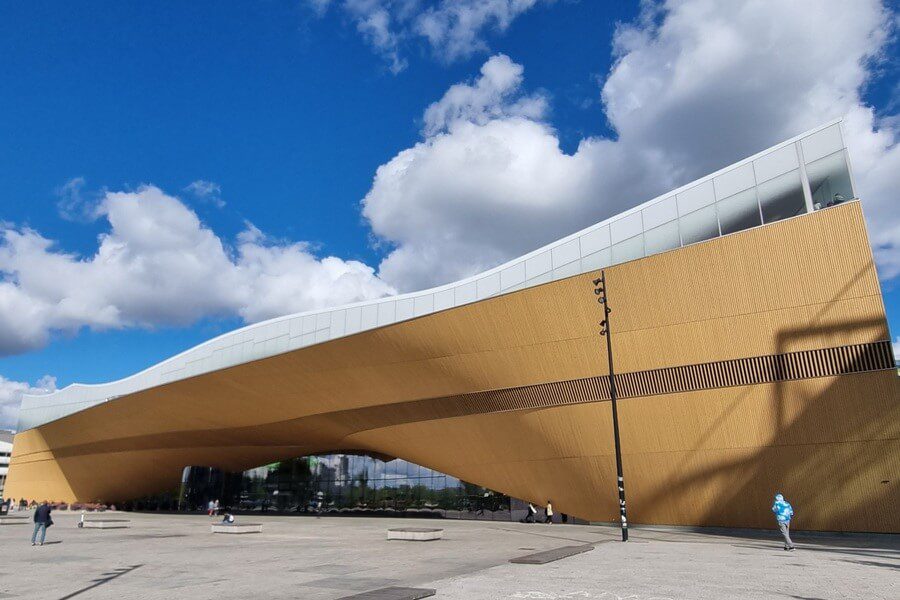 The wave-like wooden facade of Oodi Central Library in Helsinki under a blue sky, a modern architectural landmark for cultural immersion.