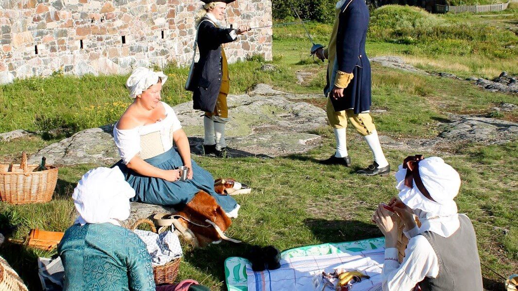 People in period costumes having a picnic at Suomenlinna sea fortress, a top cultural activity in Helsinki.