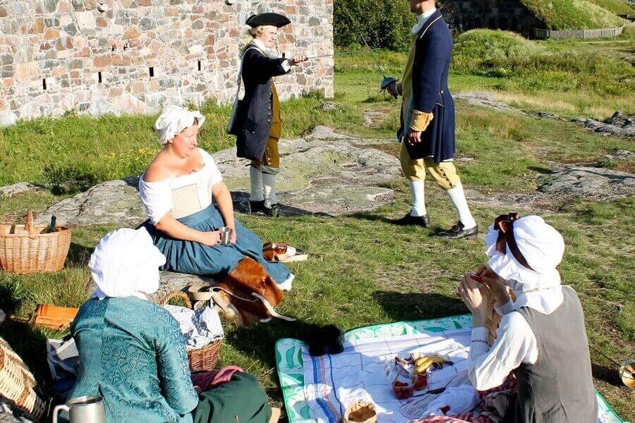 People in period costumes having a picnic at Suomenlinna sea fortress, a top cultural activity in Helsinki.