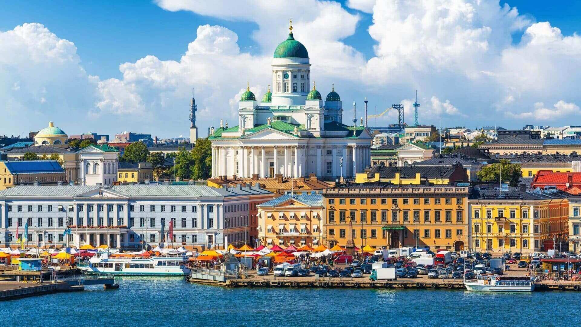 Panoramic view of the iconic white neoclassical Helsinki Cathedral with green domes overlooking the vibrant market square and bustling harbour on a sunny day.